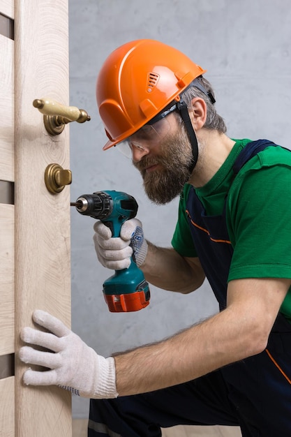 Un fabbro maschio installa una porta in un appartamento Il ragazzo lavora con un cacciavite