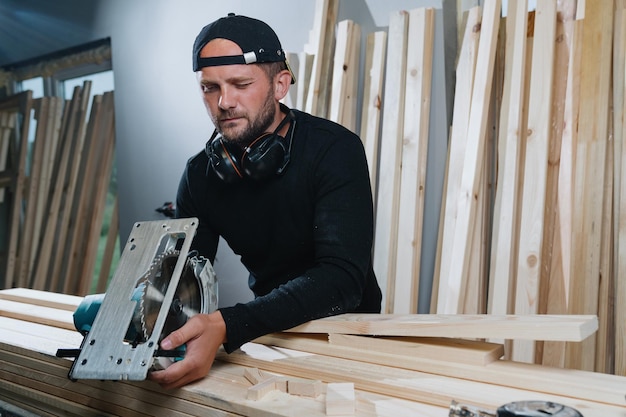 Un falegname in abiti scuri controlla l'affilatura di una lama per sega elettrica in un'officina di lavorazione del legno