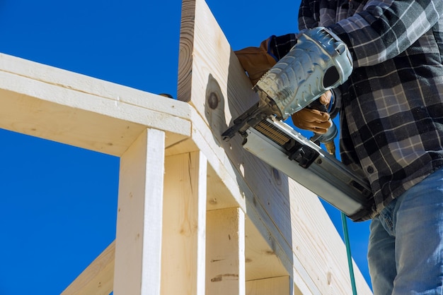 Un falegname per inchiodare trave di legno utilizzando un martello pneumatico in cantiere