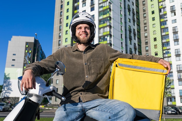 Un fattorino sorridente si siede su uno scooter dopo aver consegnato il cibo al cliente