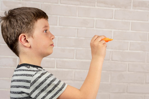 Un felice ragazzo caucasico in età scolastica scrive in aria con un pennarello arancione il concetto di studio e attività scolastiche e istruzione