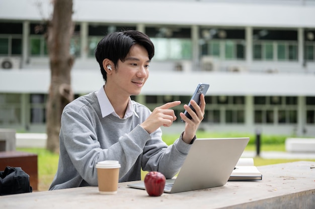 Un felice studente universitario asiatico che ascolta musica da solo in un parco del campus