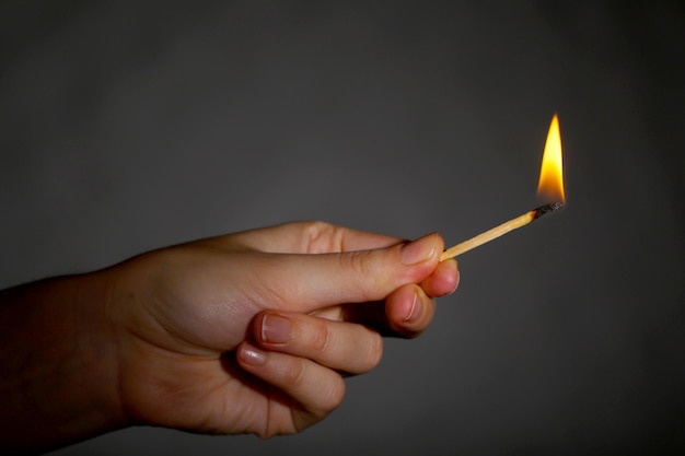 Un fiammifero in fiamme in mano su sfondo nero