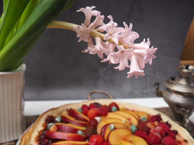 Un fiore bianco è in primo piano e una crostata di frutta è sullo sfondo.