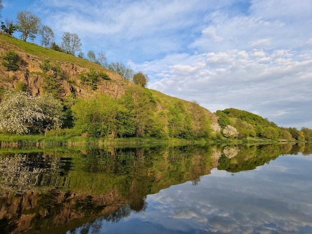 Un fiume con alberi sulla collina e un cielo azzurro con nuvole