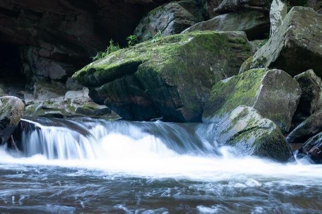 Un fiume scorre attraverso una zona rocciosa con rocce coperte di muschio e una piccola cascata.