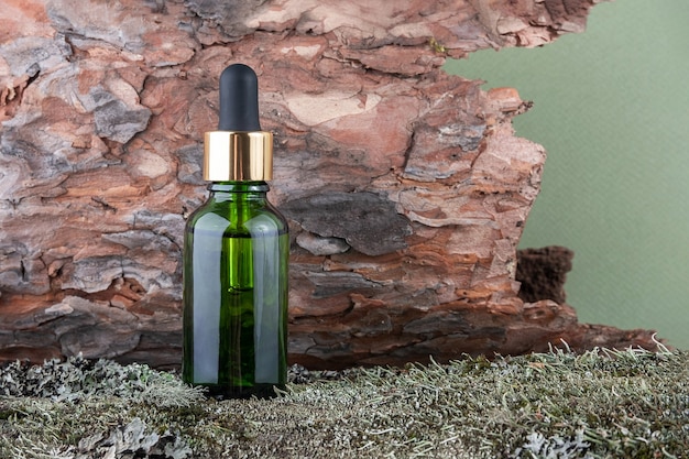 Un flacone cosmetico in vetro verde con siero, olio essenziale su sfondo verde di muschio e corteccia d'albero. Natural Organic Spa Cosmetic concept Vista frontale.