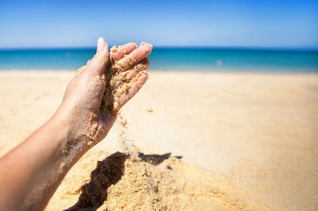 Un flusso di sabbia cade dalla mano di una donna su una spiaggia sabbiosa