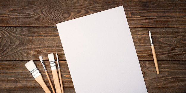 Un foglio bianco pulito e pennelli su uno sfondo strutturato con spazio da copiare. Layout, spazio mockup per testo e disegno.