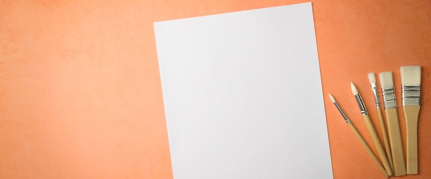 Un foglio bianco pulito e pennelli su uno sfondo strutturato con spazio da copiare. Layout, spazio mockup per testo e disegno.