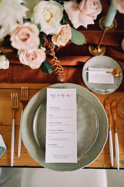Un foglio con un menu festivo giace su un piatto accanto a un bouquet di fiori sul tavolo