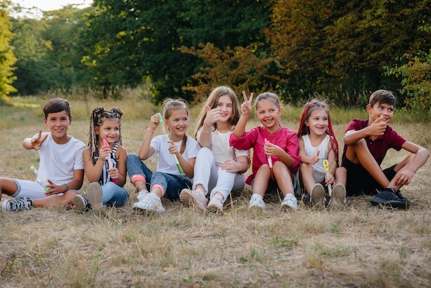 Un folto gruppo di bambini allegri si siede sull'erba del Parco e sorride. Giochi in un campo per bambini.