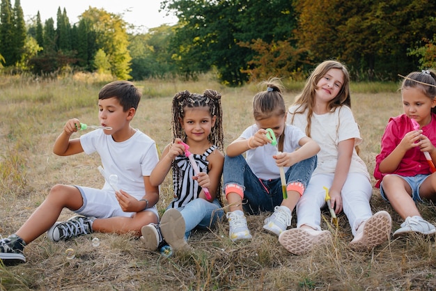 Un folto gruppo di bambini allegri si siede sull'erba del Parco e sorride. Giochi in un campo per bambini.