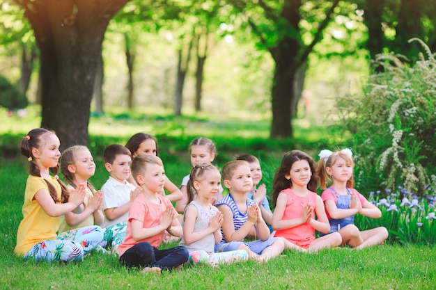 Un folto gruppo di bambini impegnati nello yoga nel parco seduto sull'erba.