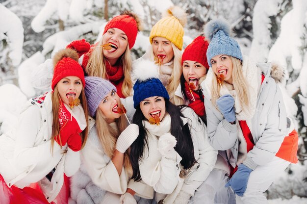 Un folto gruppo di ragazze con lecca-lecca in mano si trova nella foresta invernale. Ragazze in abiti rossi e bianchi con caramelle in una foresta innevata.