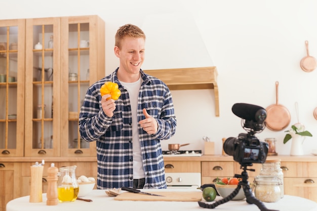 Un food blogger crea contenuti e guarda la telecamera Un cuoco maschio tiene in mano un peperone giallo e annuisce alla telecamera