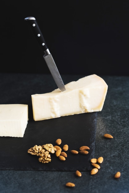 Un formaggio solido appetitoso su una piastra nera con coltello, mandorle e noci