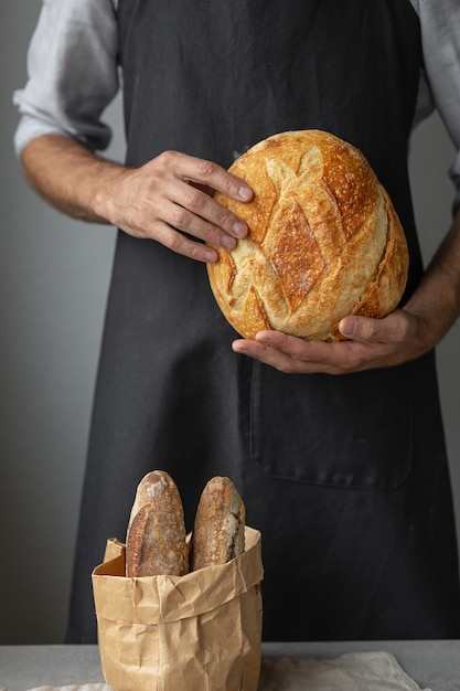 Un fornaio maschio europeo adulto tiene in mano un pane fresco rotondo un uomo in una panetteria tiene a