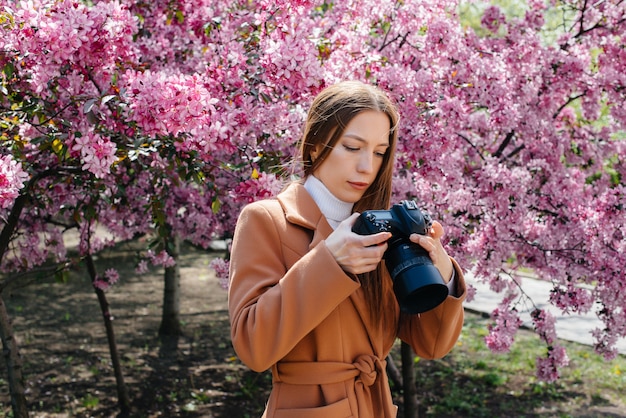 Un fotografo giovane e bella ragazza cammina e scatta foto contro un albero di mele in fiore. Interessi, ricreazione.
