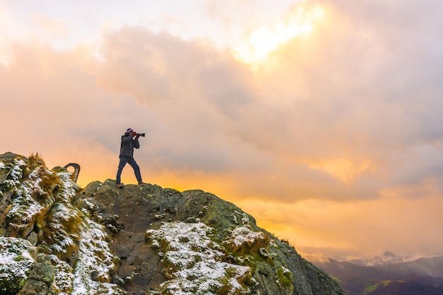 Un fotografo in cima alla montagna in inverno nevoso tramonto arancione, sul monte Peñas de Aya nella città di Oiartzun vicino a San Sebastian, Spagna