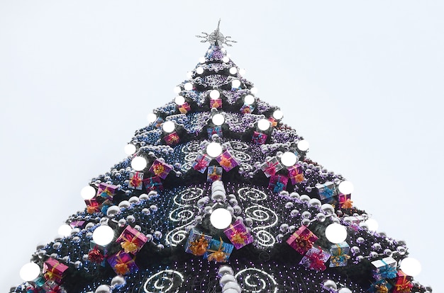 Un frammento di un enorme albero di Natale con molti ornamenti, scatole regalo e lampade luminose