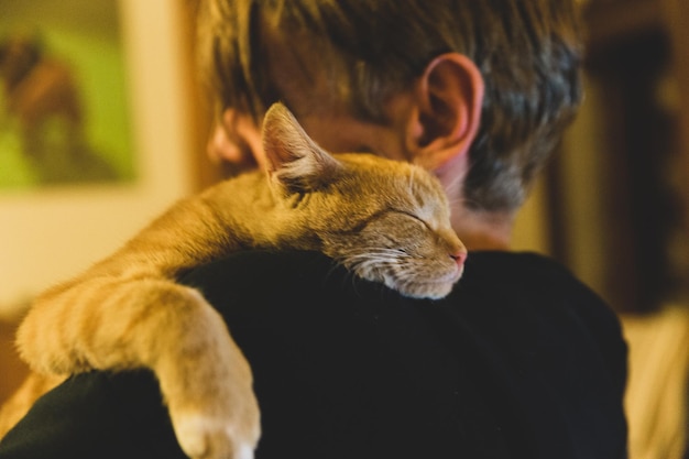 Un gatto rosso addormentato giace sulla spalla di un uomo biondo