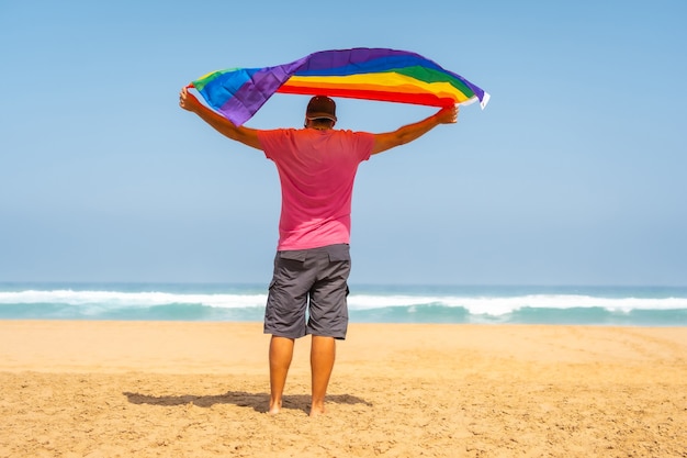 Un gay con una maglietta rosa e un berretto nero con la bandiera LGBT su una spiaggia, simbolo dell'omosessualità