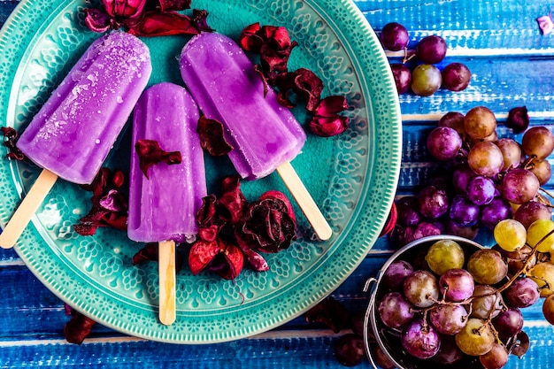 Un gelato all'uva in stile Lollipop su un bastoncino su un piatto vintage su un tavolo di legno azzurro Concetto di mangiare sano e naturale Copyspace