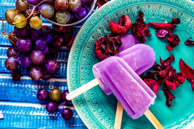 Un gelato all'uva in stile Lollipop su un bastoncino su un piatto vintage su un tavolo di legno azzurro Concetto di mangiare sano e naturale Copyspace