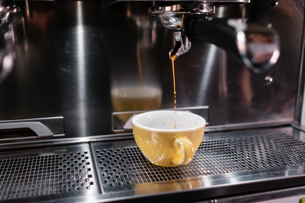 Un getto di caffè che versa in una tazza Gocce di caffè del primo piano Processo di preparazione del caffè