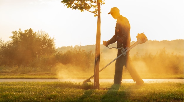 Un giardiniere falcia il prato con un tosaerba la mattina presto all'alba