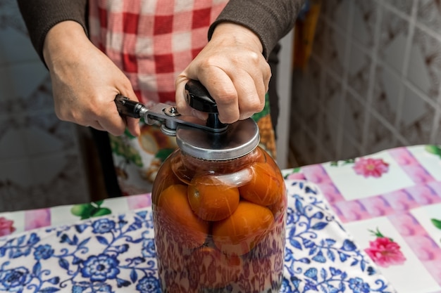 Un giardiniere femminile prepara i pomodori salati. Li avvolge in barattoli di vetro.