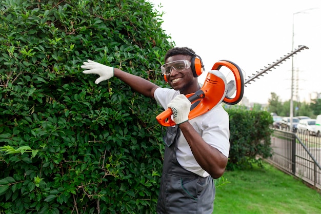 Un giardiniere in uniforme taglia cespugli un uomo afroamericano con occhiali e cuffie