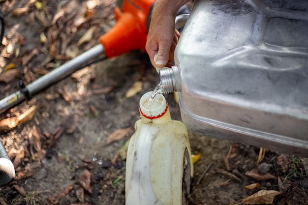 Un giardiniere versa benzina da una lattina in un contenitore di plastica per riempire una falciatrice