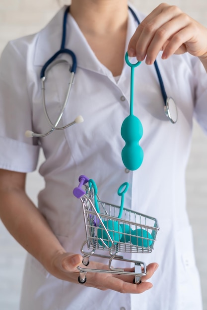 Un ginecologo senza volto mette una serie di palline vaginali in un carrello della spesa in miniatura Il medico tiene in mano un mini carrello e un dispositivo per i muscoli del pavimento pelvico Concetto di salute femminile Giocattolo di Kegel