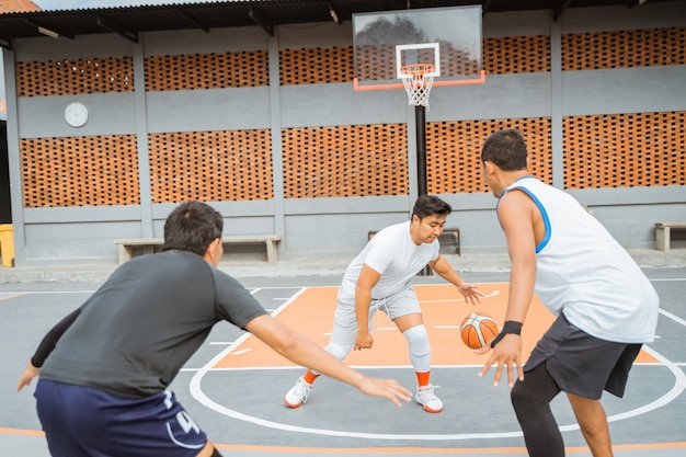 Un giocatore di basket maschile con una tuta da ginnastica bianca dribbla la palla di fronte a due giocatori avversari