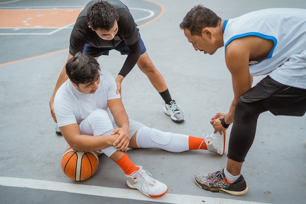 Un giocatore di basket si siede a terra a causa di un crampo muscolare ed è aiutato da un altro giocatore