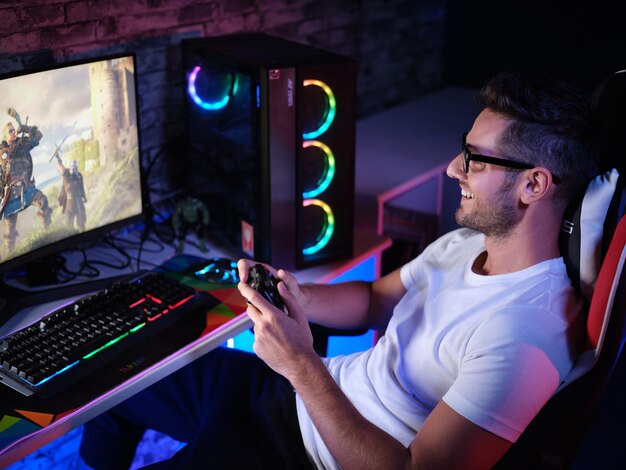 Un giocatore gioioso gioca su PC sorridendo ampiamente e tenendo in mano un telecomando di gioco mentre è circondato da Sparkli