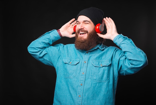 Un gioioso giovane hipster sta ascoltando la musica che ama con le sue nuove cuffie e si diverte a guardare lontano