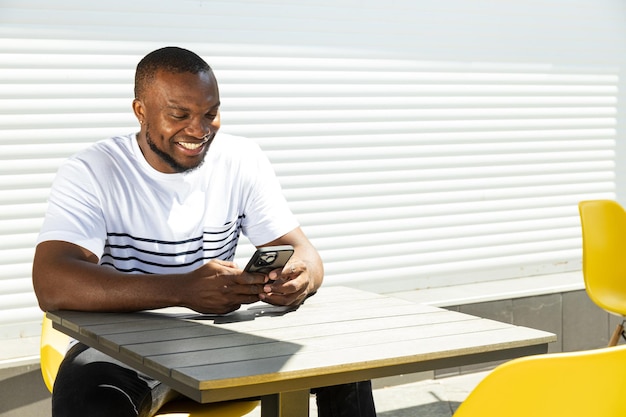 Un giovane afroamericano con uno smartphone in mano è seduto a un tavolo