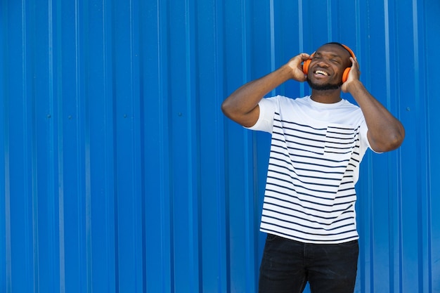 Un giovane afroamericano elegante ascolta musica in cuffia su uno sfondo blu