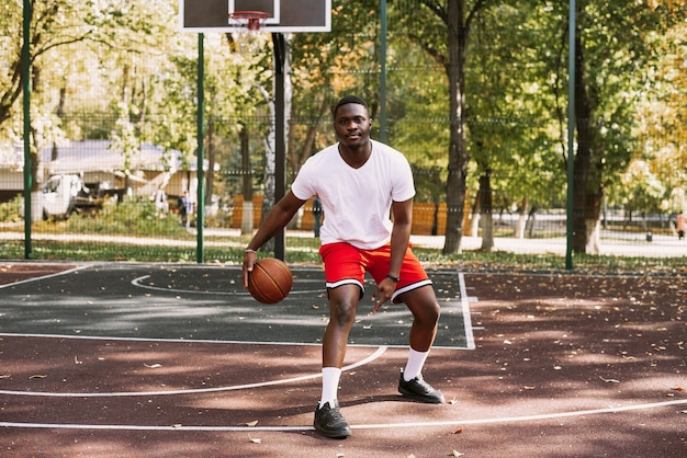 Un giovane afroamericano sta giocando a basket su un campo all'aperto, sorridendo e guardando la telecamera. Sport all'aperto.