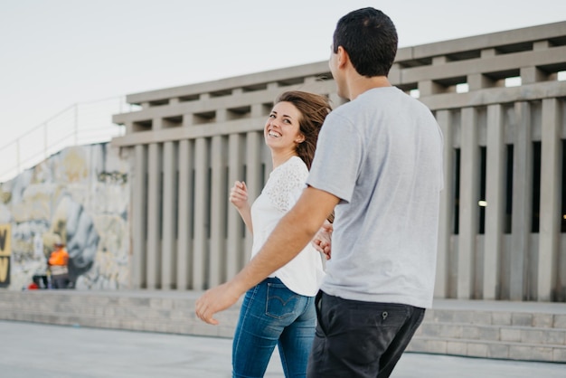 Un giovane alla moda si tiene per mano con la sua ragazza bruna nel porto