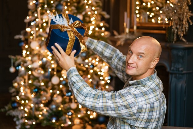 Un giovane allegro caucasico di buon umore posa con un regalo incartato vicino a un c...