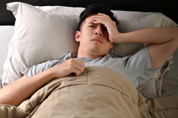 Un giovane asiatico depresso sdraiato a letto non riesce a dormire per l'insonnia