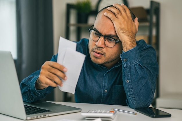 Un giovane asiatico è stressato perché guarda molte spese e non ha soldi da pagare