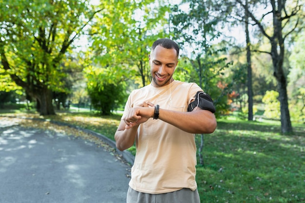 Un giovane atleta afroamericano maschio è in piedi nel parco e sta andando a correre aggiusta una smart