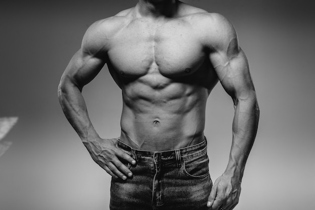 Un giovane atleta sexy con addominali perfetti posa in studio in topless in jeans. Stile di vita sano, corretta alimentazione, programmi di allenamento e alimentazione per dimagrire. Bianco e nero.