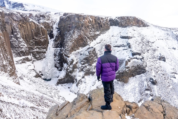 Un giovane avventuroso che guarda la cascata ghiacciata di Hengifoss in inverno in Islanda