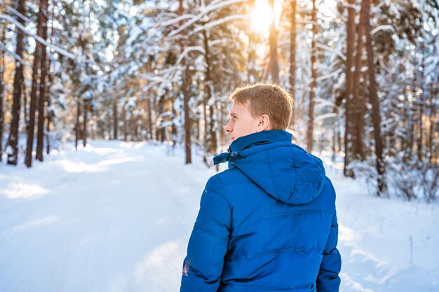 Un giovane biondo in una foresta di neve di abete rosso in una giornata di sole in inverno Bella natura escursionismo invernale